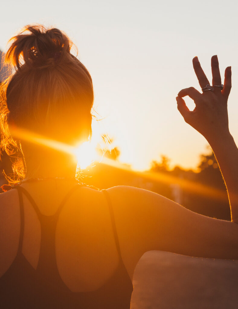 Mädchen steht in der Sonne und formt mit Daumen und Zeigefinger ein Handzeichen.